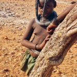 La jeune fille Himba se reconnait notamment grâce à son crâne rasé sur les côtés et deux longues tresses qui retombent sur le devant.