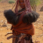Cette femme porte une jupe en peau ou « Ombanda ». Elle arbore aussi l’epando, une ceinture qui indique qu’elle a eu des enfants.