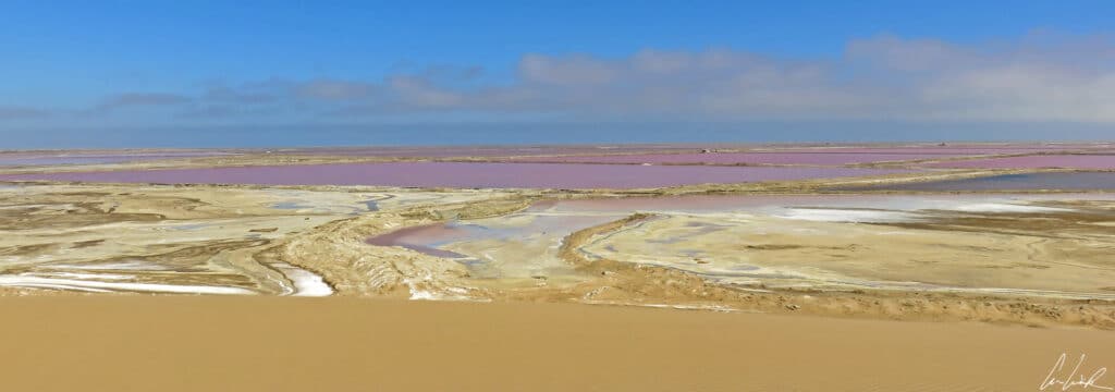 In the middle of the orange sand dunes, the Walvis Bay salt fields form a mosaic of pink pools under an azure blue sky.