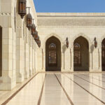 Le bâtiment central de la Grande Mosquée du Sultan Qaboos est entouré au nord et au sud par des couloirs à arcades, ornés de mosaïques et de lanternes ciselées.