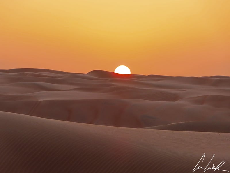 Aux premières heures du jour, les dunes du Wahiba Sands se colorent de dégradés d’orange sous un ciel lui aussi orangé.