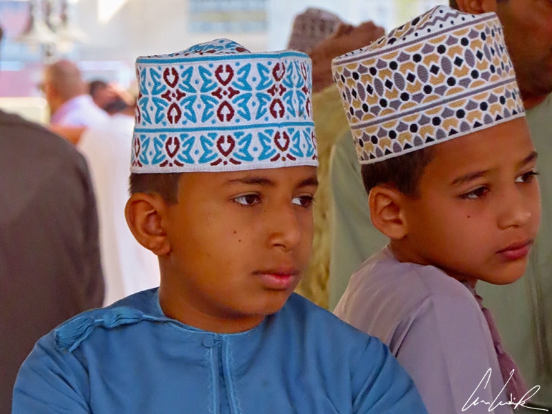 These two young children are wearing the traditional round embroidered hat: the kumma. It matches their dishdasha: blue for one and purple for the other.