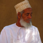 This elder with a grey beard wears a white dishdasha on which hangs on the right side the little pompom called tarboucha.