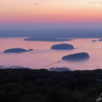 Daylight rises on the calm waters of Frenchman Bay in Acadia National Park. A thin mist envelops the Porcupine Islands.