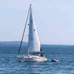 Un voilier croise au large du phare de Bass Harbor, propulsé par la force du vent ou par son moteur ?