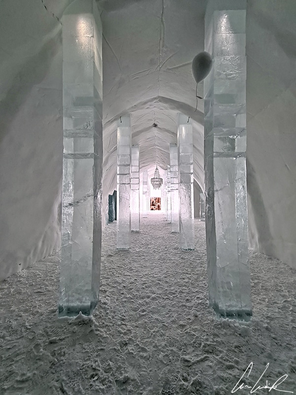 L’immense couloir du IceHotel de Jukkasjärvi est fait d’une succession de voûtes de neige et de grandes colonnes de glaces pour soutenir l’ensemble. Au bout du couloir de neige, la porte d’entrée laisse passer la lumière.