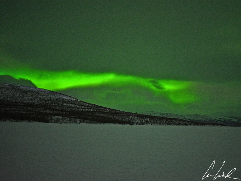 Observation des aurores boréales à Abisko en Laponie suédoise. Un vert intense illumine les montagnes enneigées.