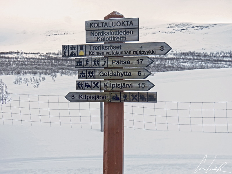 Panneau en bois indiquant la direction le Trerikroset, le rocher symbolique qui marque la frontière des trois pays nordiques, près de Kilpisjärvi