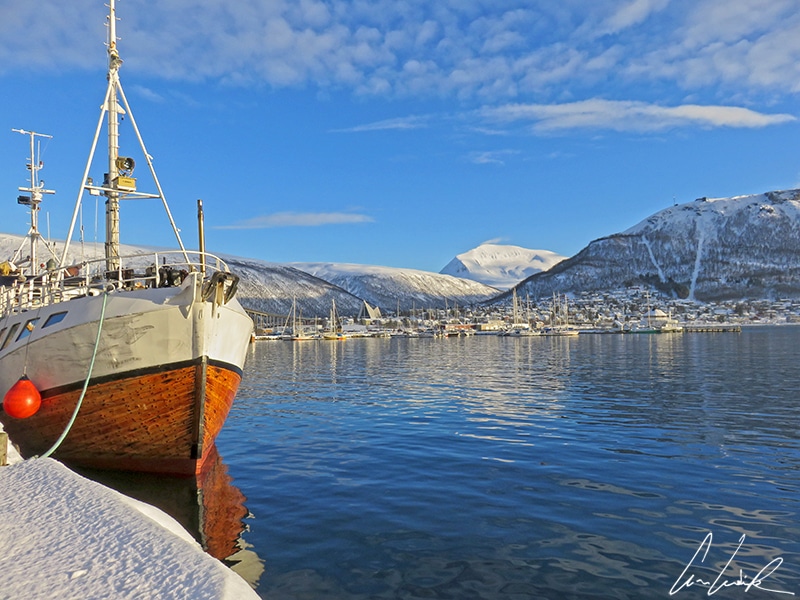 La baie de Tromsø avec ses navires de pêche et en arrière plan la cathédrale arctique (Ishavskatedralen) et le téléphérique Fjellheisen qui relie Tromsø au sommet de la montagne Storsteinen.