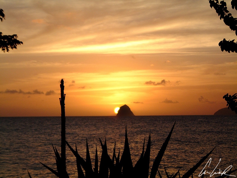 In Martinique, the beach of Diamant is beautiful at sunset when an orange light bathes the shore with the Diamond rock in the background.