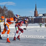 Sea-Ice marathon skaters glide at full speed on the isbana of Luleå. In the background, we see the city and Luleå Cathedral.