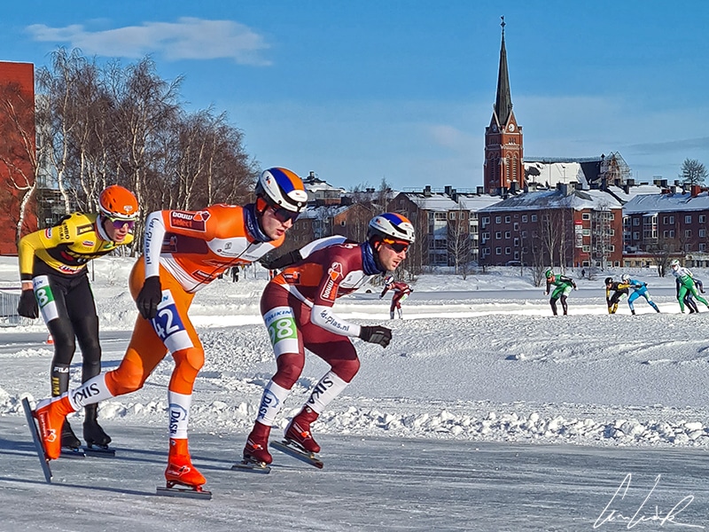 Sea-Ice marathon skaters glide at full speed on the isbana of Luleå. In the background, we see the city and Luleå Cathedral.